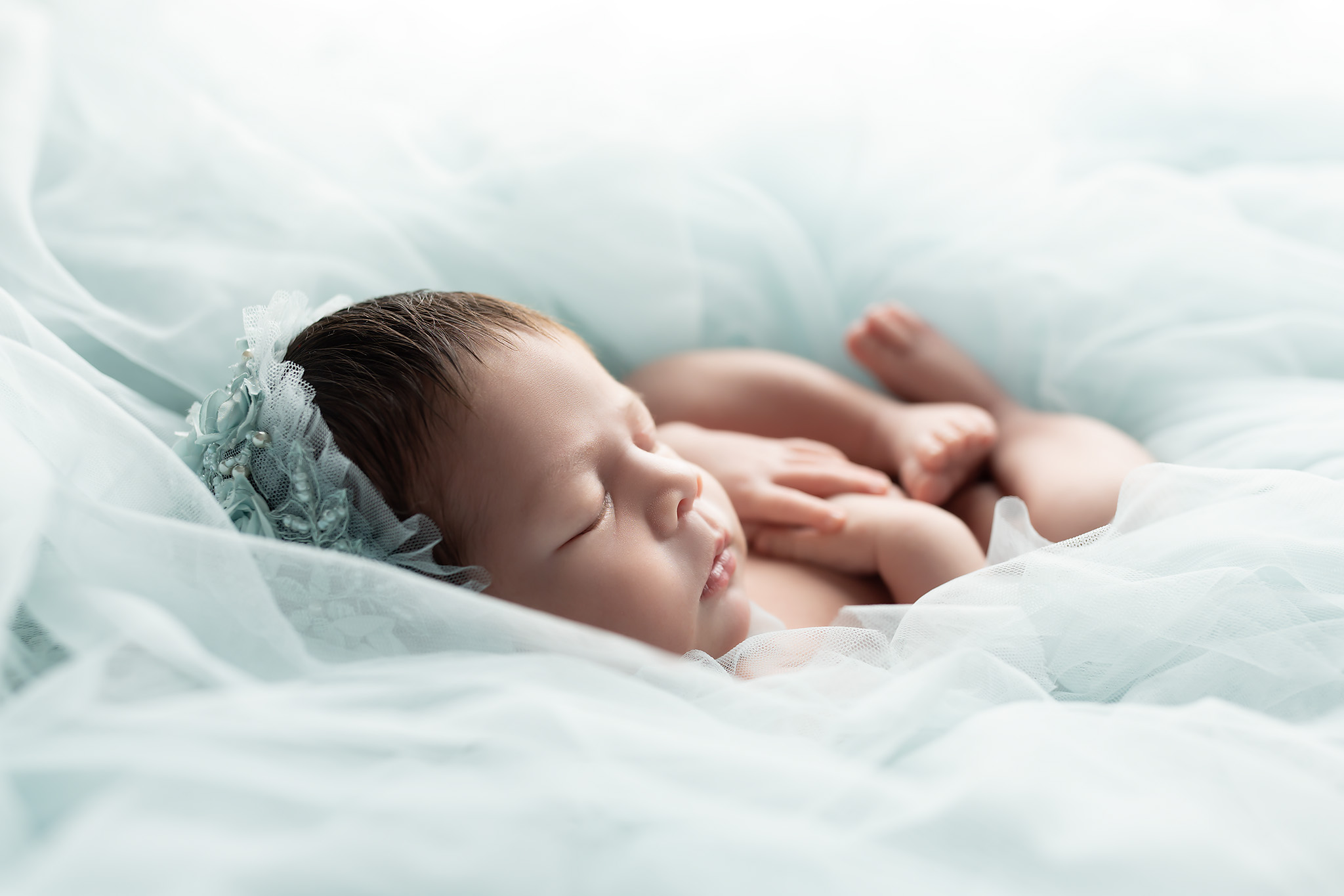 Lovely baby girl surrounded by soft green tulle and beautiful lighting. Helping you know When to Schedule Your Newborn Photoshoot in Dallas
