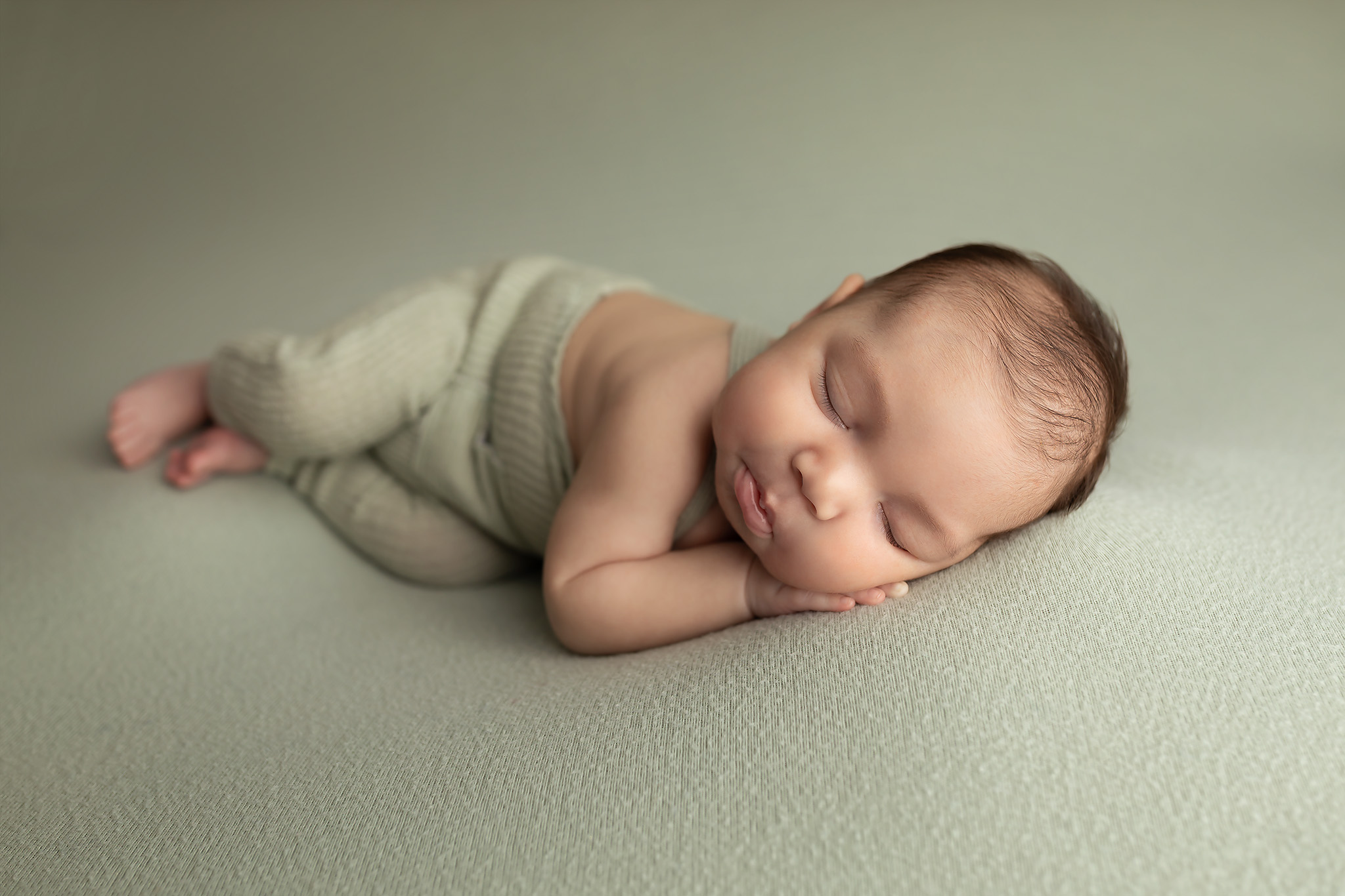Baby boy resting on his side in a green outfit on a soft green backdrop.
