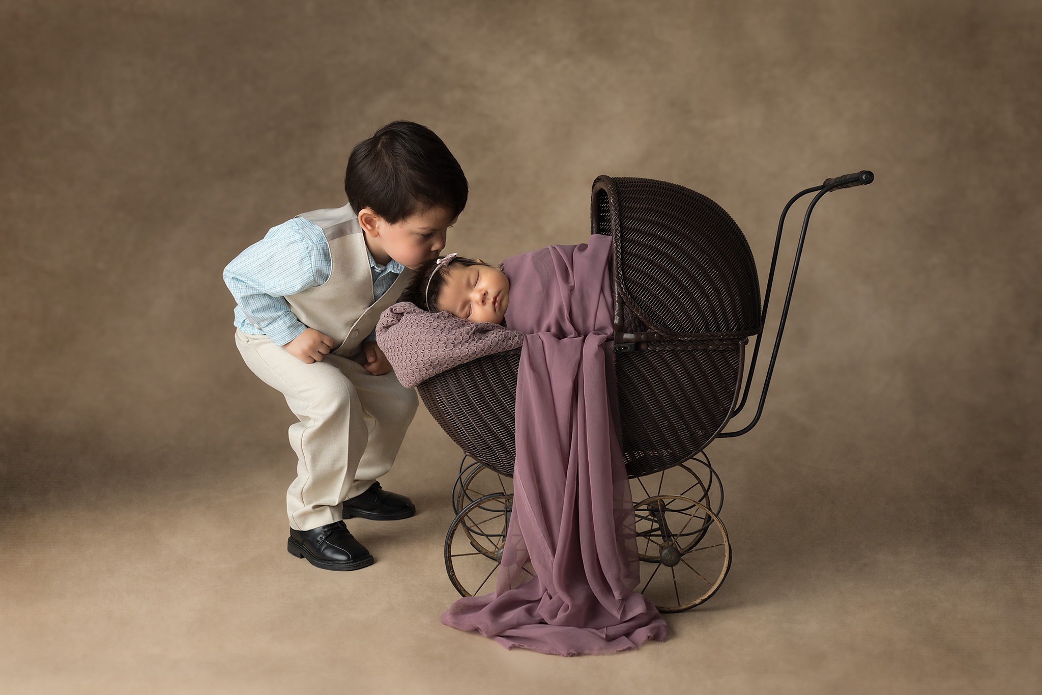 professional photo of young child kissing forehead of newborn in pram