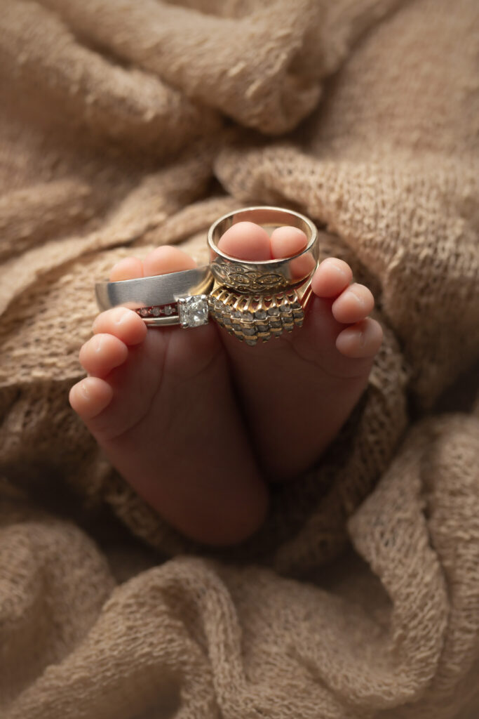 Newborn baby with mother and father's rings on their little toes.