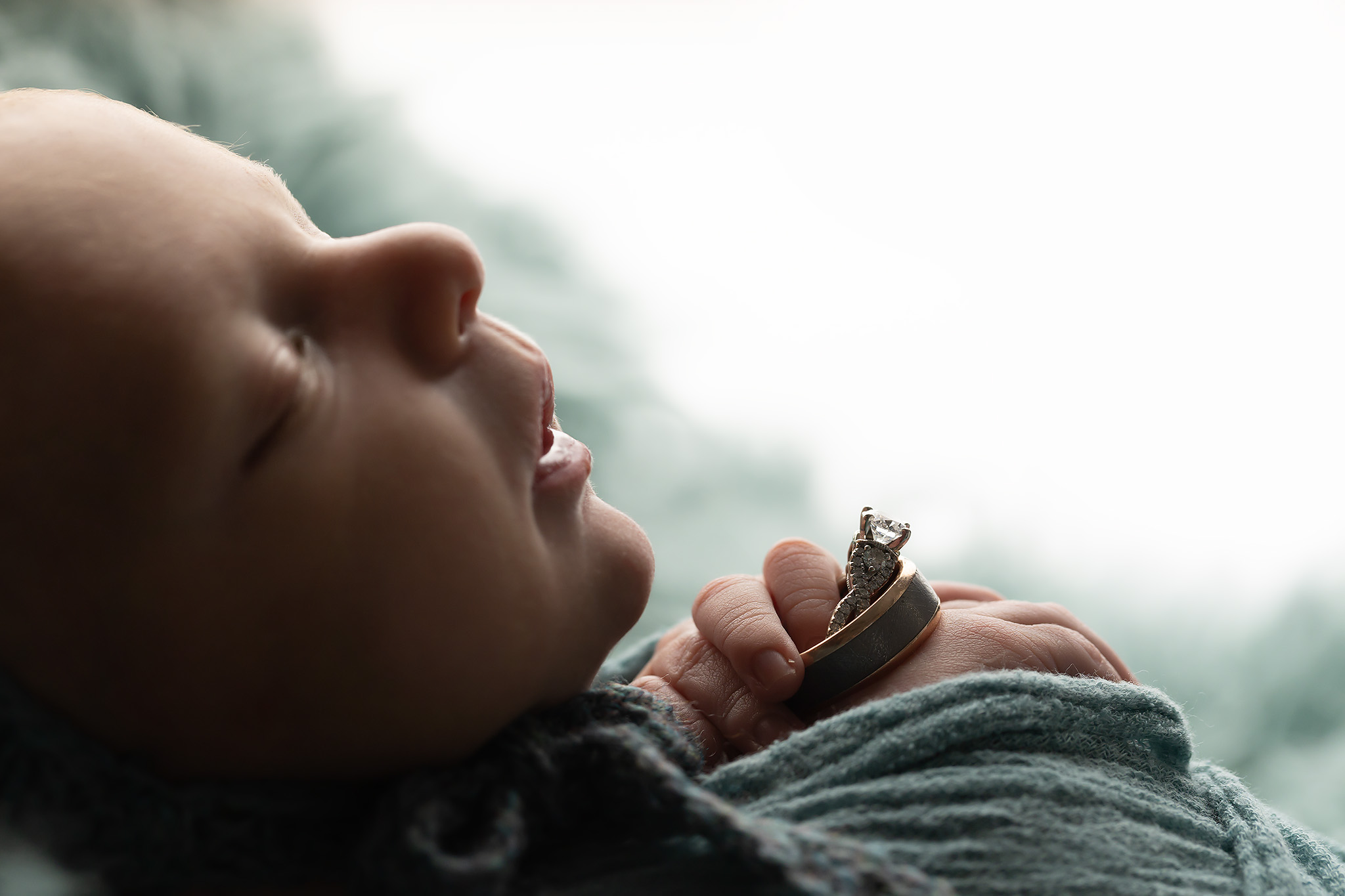 Profile of newborn baby boy holding parents' wedding rings.