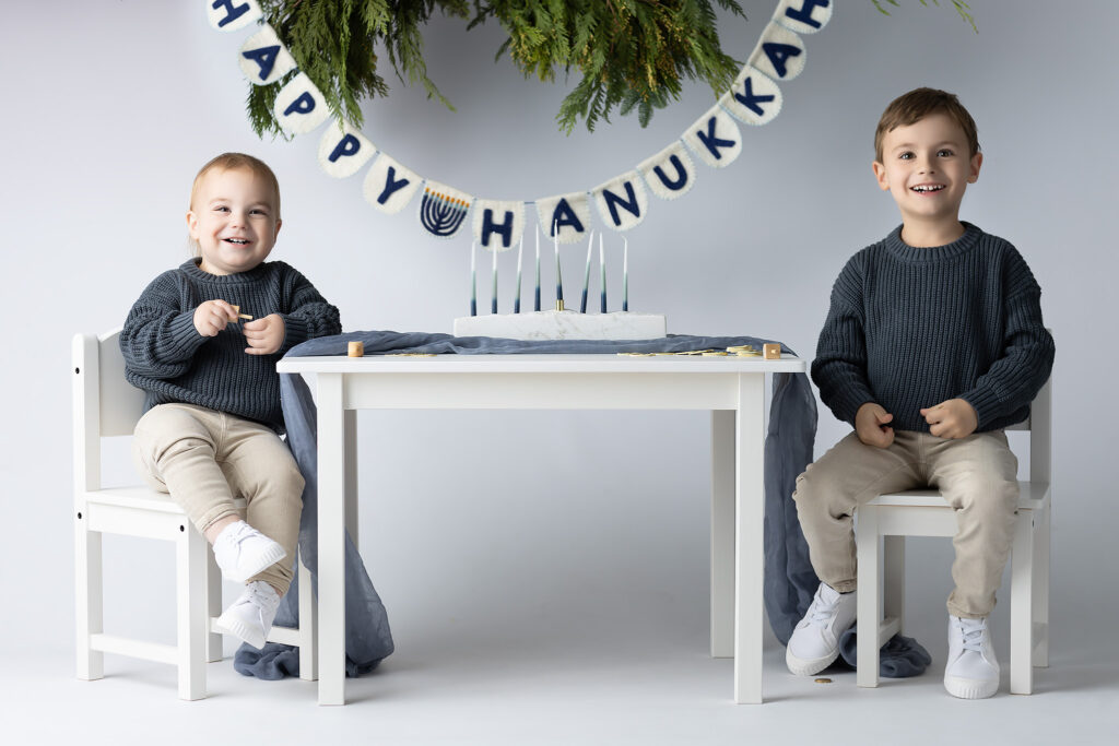 Picture of two little brothers sitting at a table with a Happy Hanukkah banner behind them.