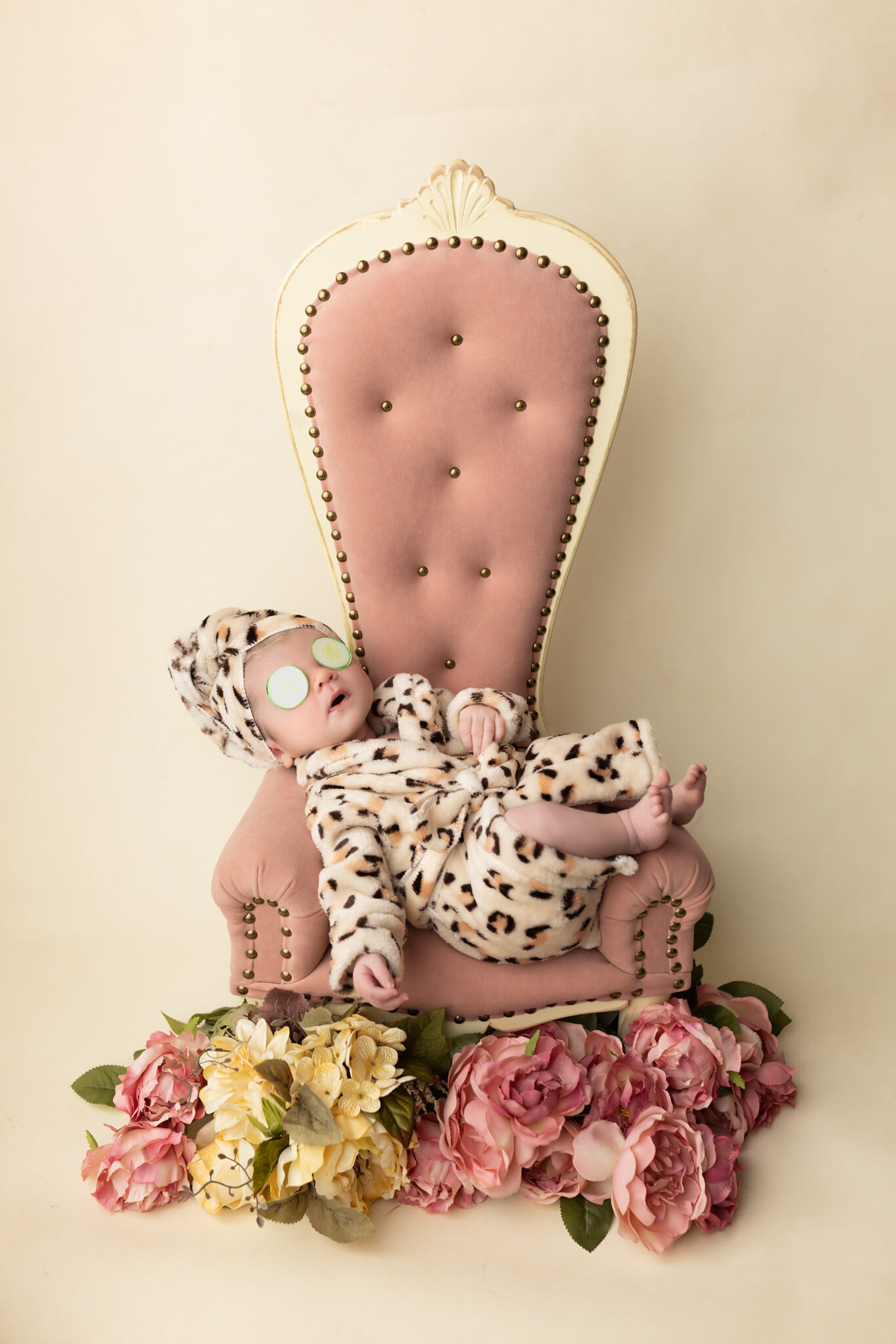 A newborn baby sleeps in a cheetah robe across a pink chair with cucumbers on her eyes after visiting dallas daycares
