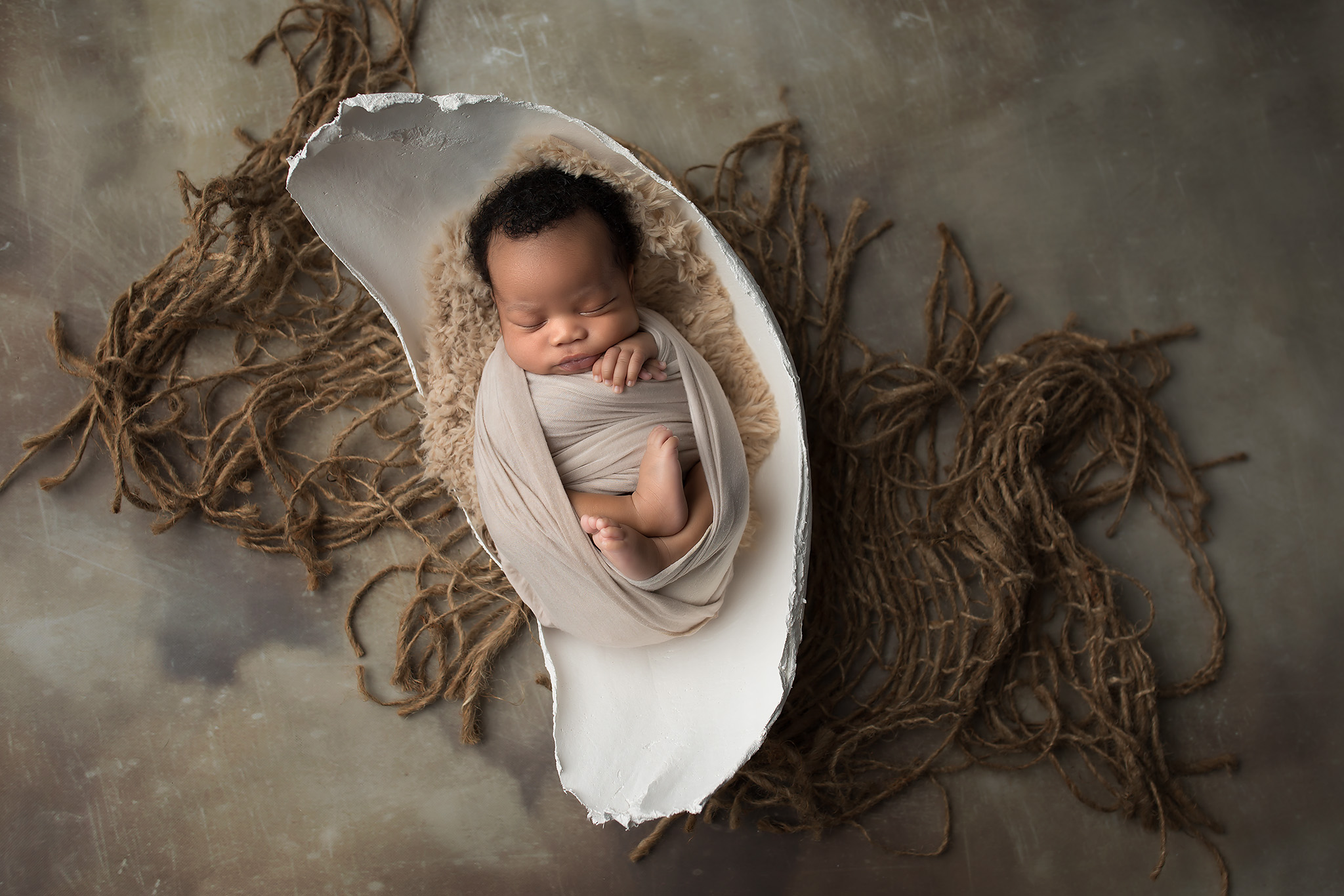 A sleeping newborn baby in a plaster bowl on a net in a studio after visiting dallas daycares