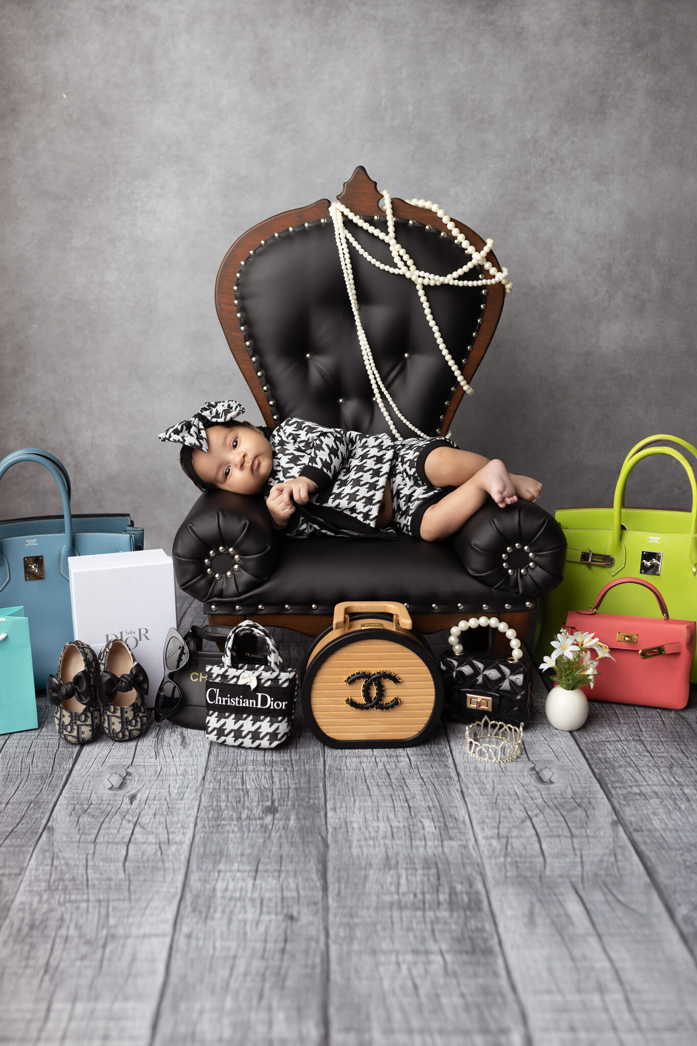A baby girl lays in a black and white outfit on a black leather chair surrounded by luxury handbags after meeting a night nanny in dallas