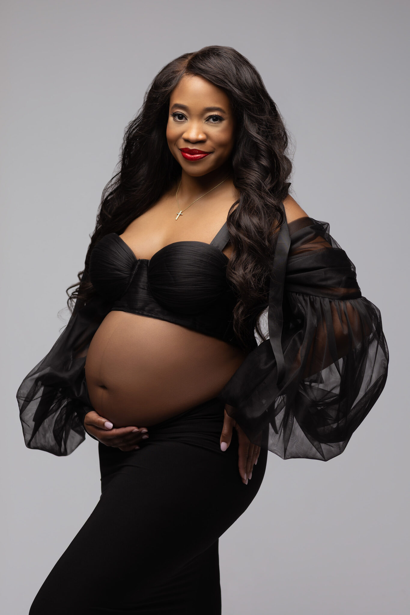 A smiling mother to be stands in a black skirt and blouse with bump out and hand under it after meeting prenatal chiropractors in fort worth