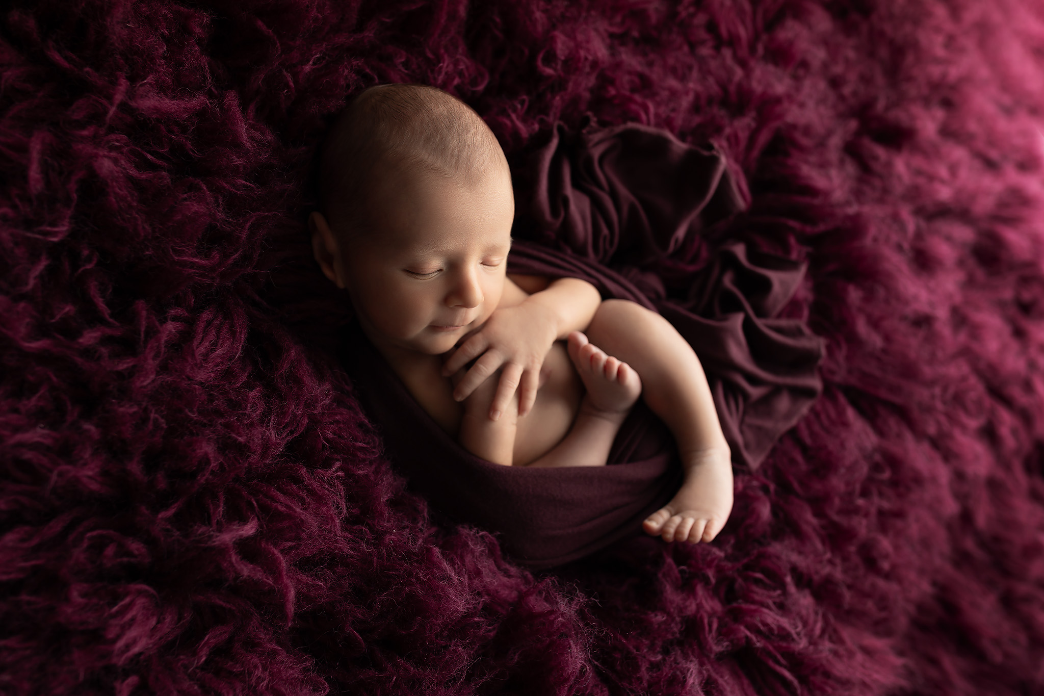 A newborn baby sleeps wrapped in an open swaddle on a purple shag blanket after meeting sleep consultants in fort worth