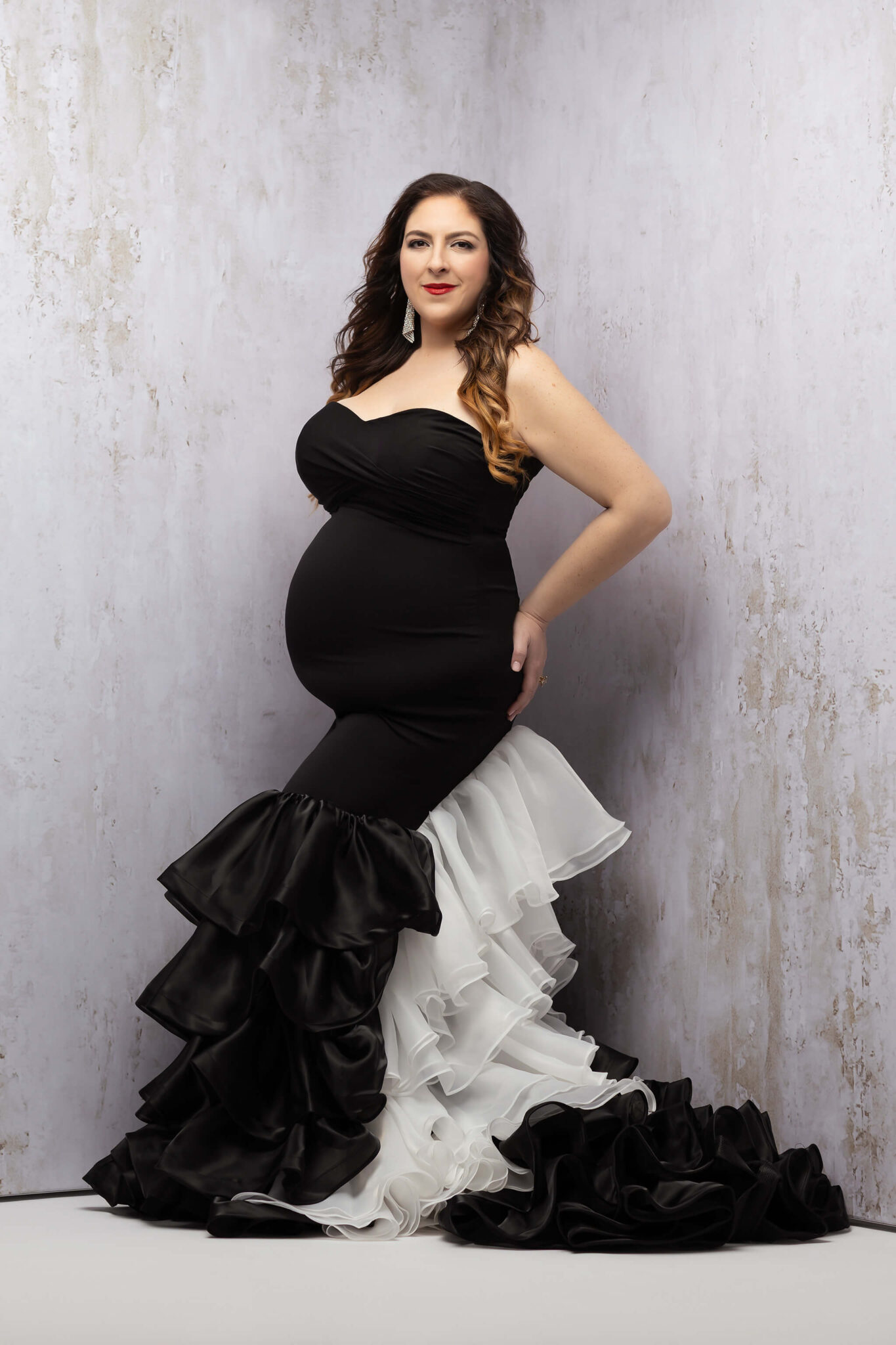A mother to be stands in a black and white maternity gown as it flows around her with a hand on her hip