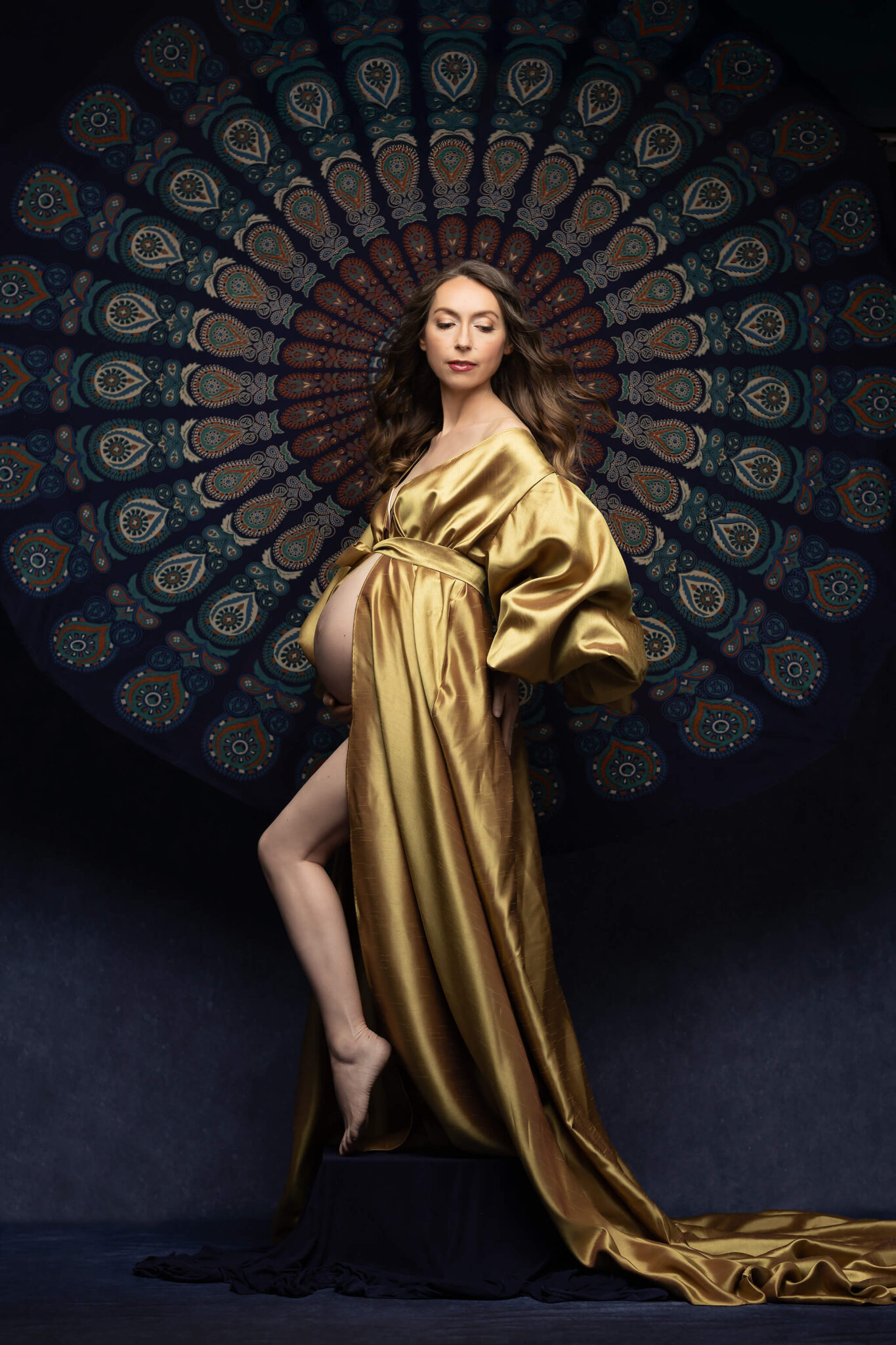 A mom to be in a gold robe walks in a studio with bump out looking down to her train after visiting birthing centers in dallas