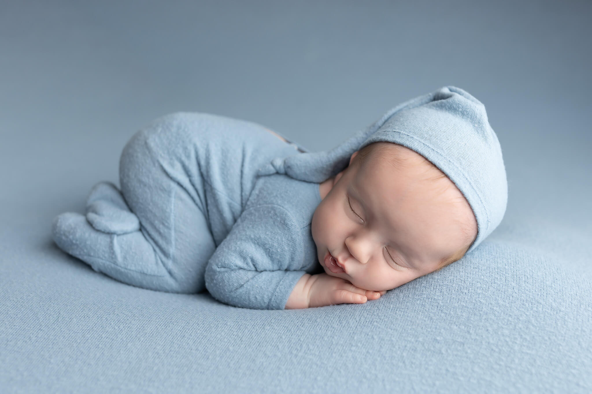 A newborn baby sleeps in froggy pose in blue pajamas and matching sleep cap after visiting infant daycares in fort worth