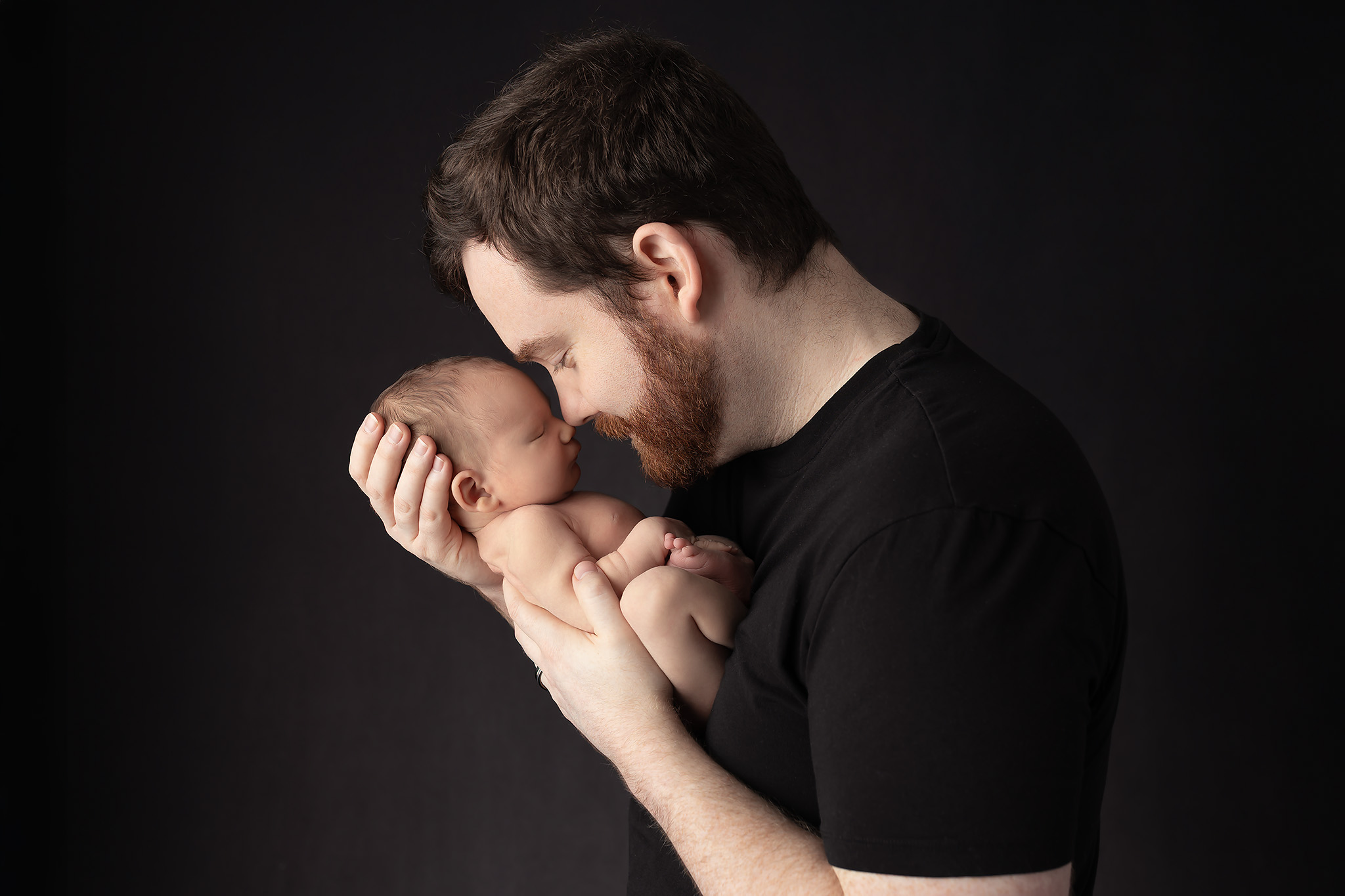 A new father in a black shirt touches noses with his sleeping newborn in his hands after some parenting classes in fort worth