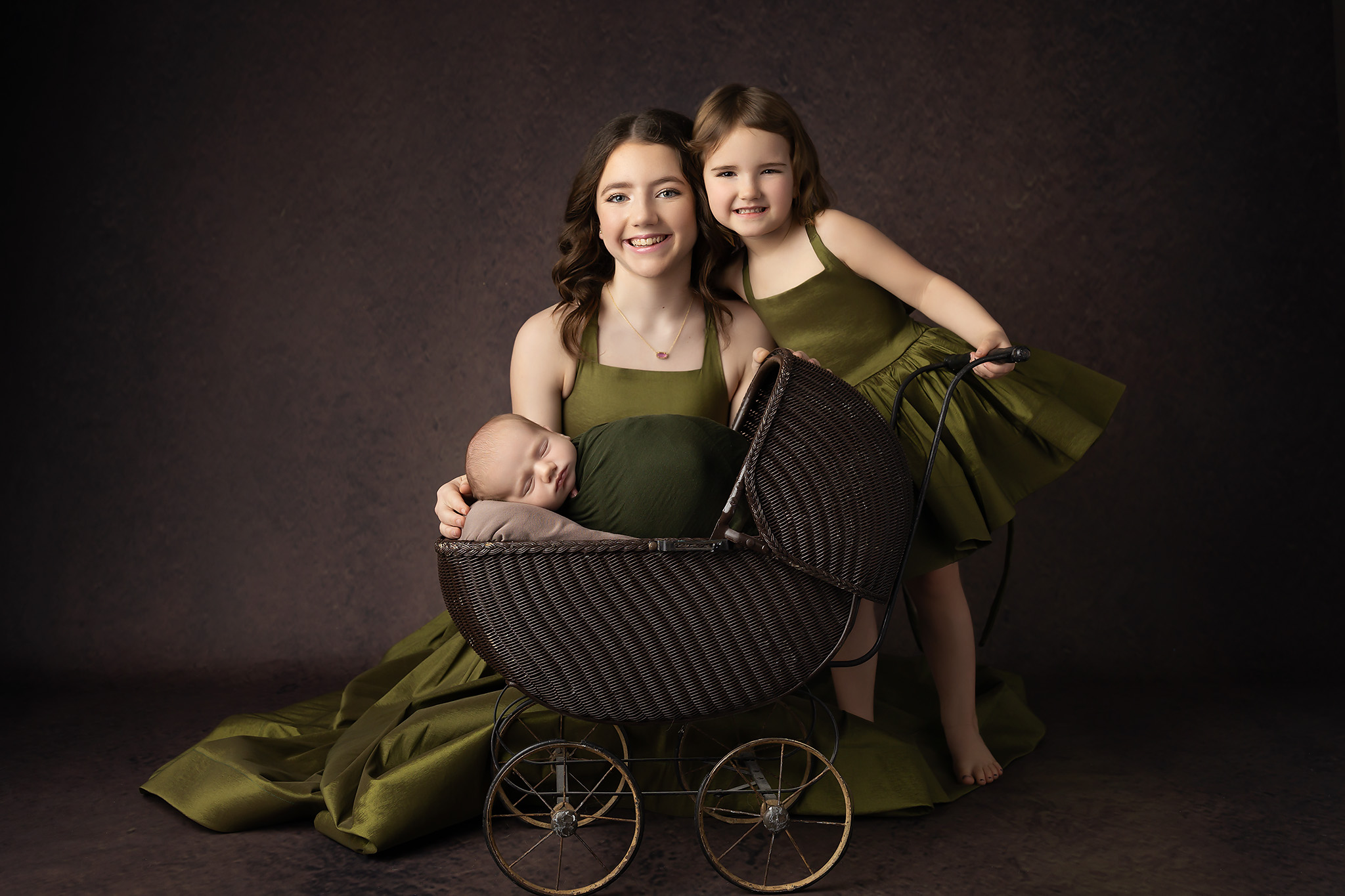 A teen girl smiles with her toddler sister in a matching green dress as they stand behind their sleeping newborn baby in a carriage after visiting pediatricians in fort worth