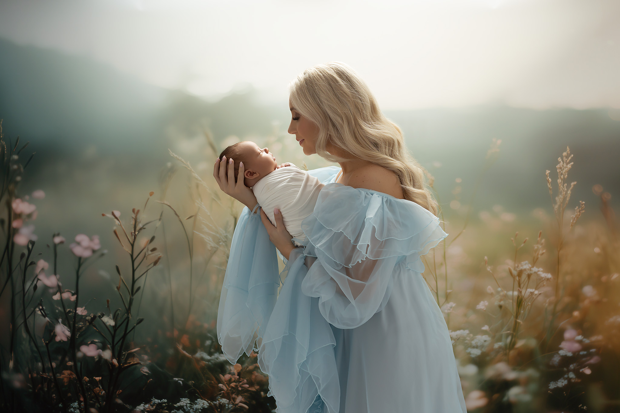 A happy new mom in a baby blue gown leans in to kiss her sleeping newborn in her hands after some pelvic floor therapy in fort worth