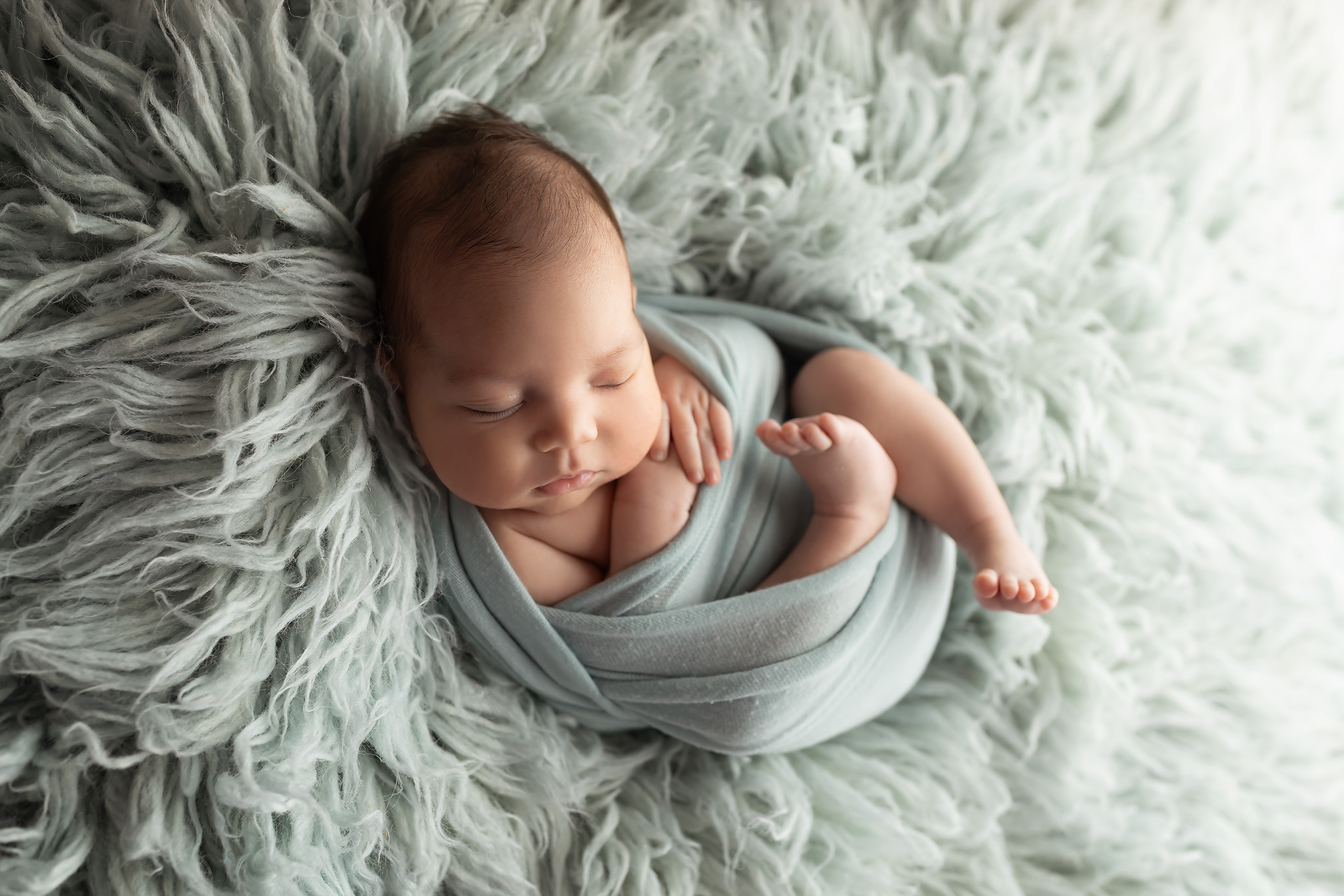 A newborn baby sleeps in a swaddle on a fur blanket in a studio