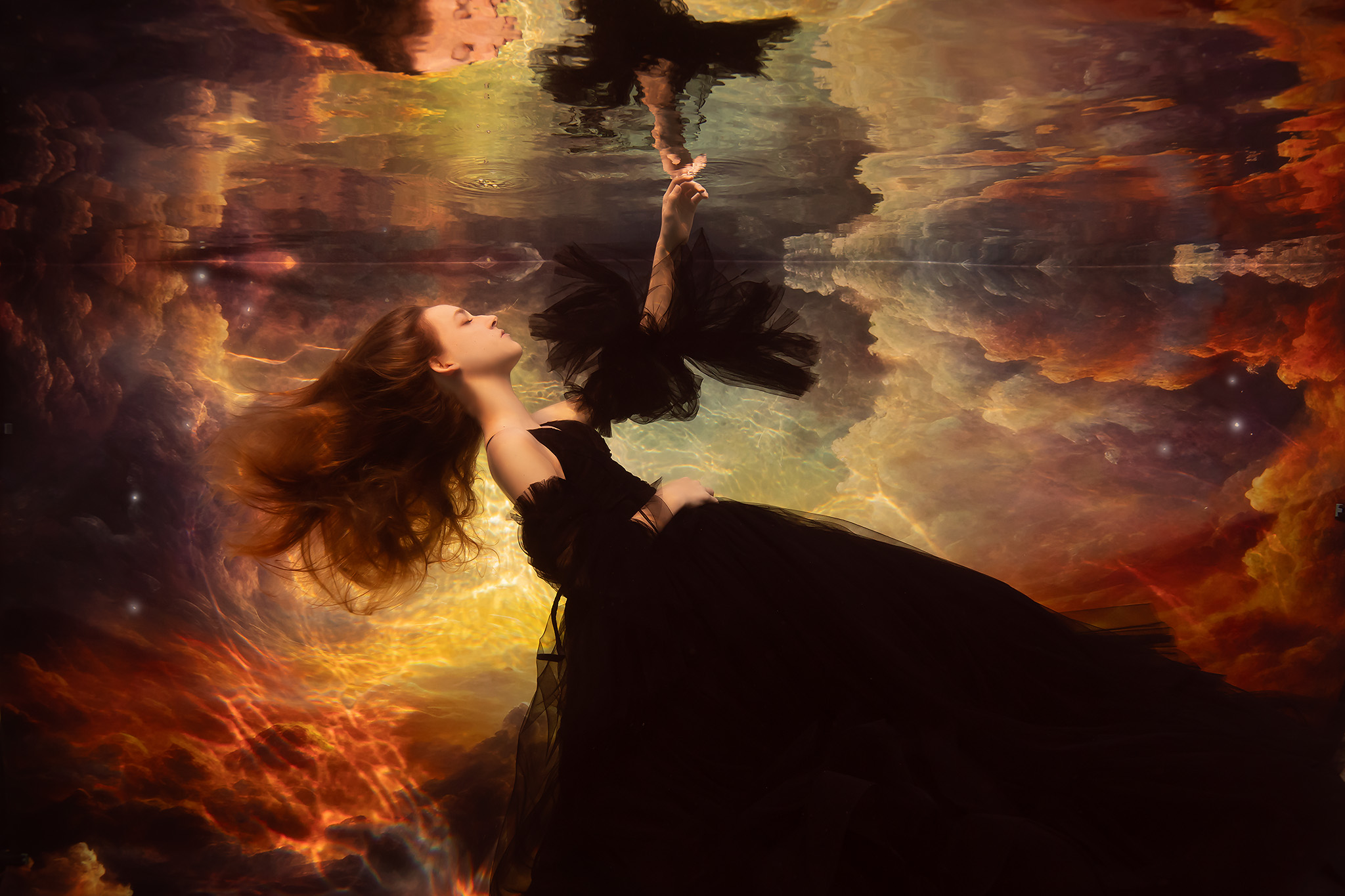Ethereal underwater senior photo session with girl in a black tulle gown in front a reflected sky backdrop