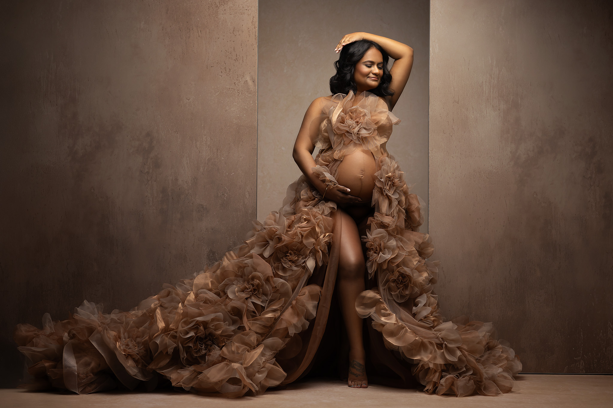 For the pregnant woman looking for a High End Photographer in Dallas this image show a woman in a long floral gown posing dramatically in front of a tan backdrop.