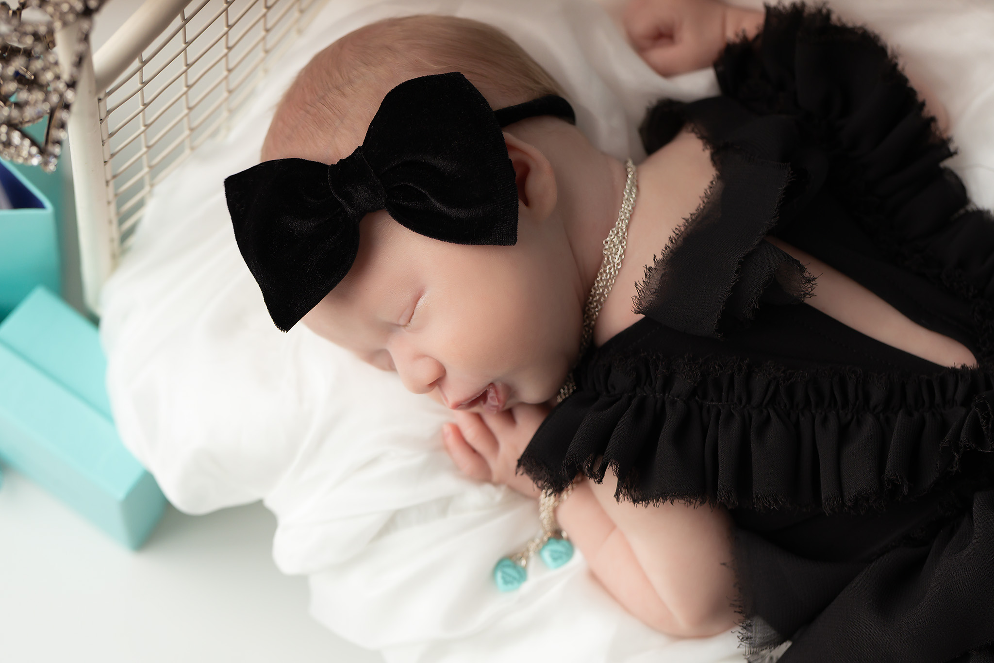 Newborn posed in a fancy black outfit with black bow wearing a Tiffany & Co necklace