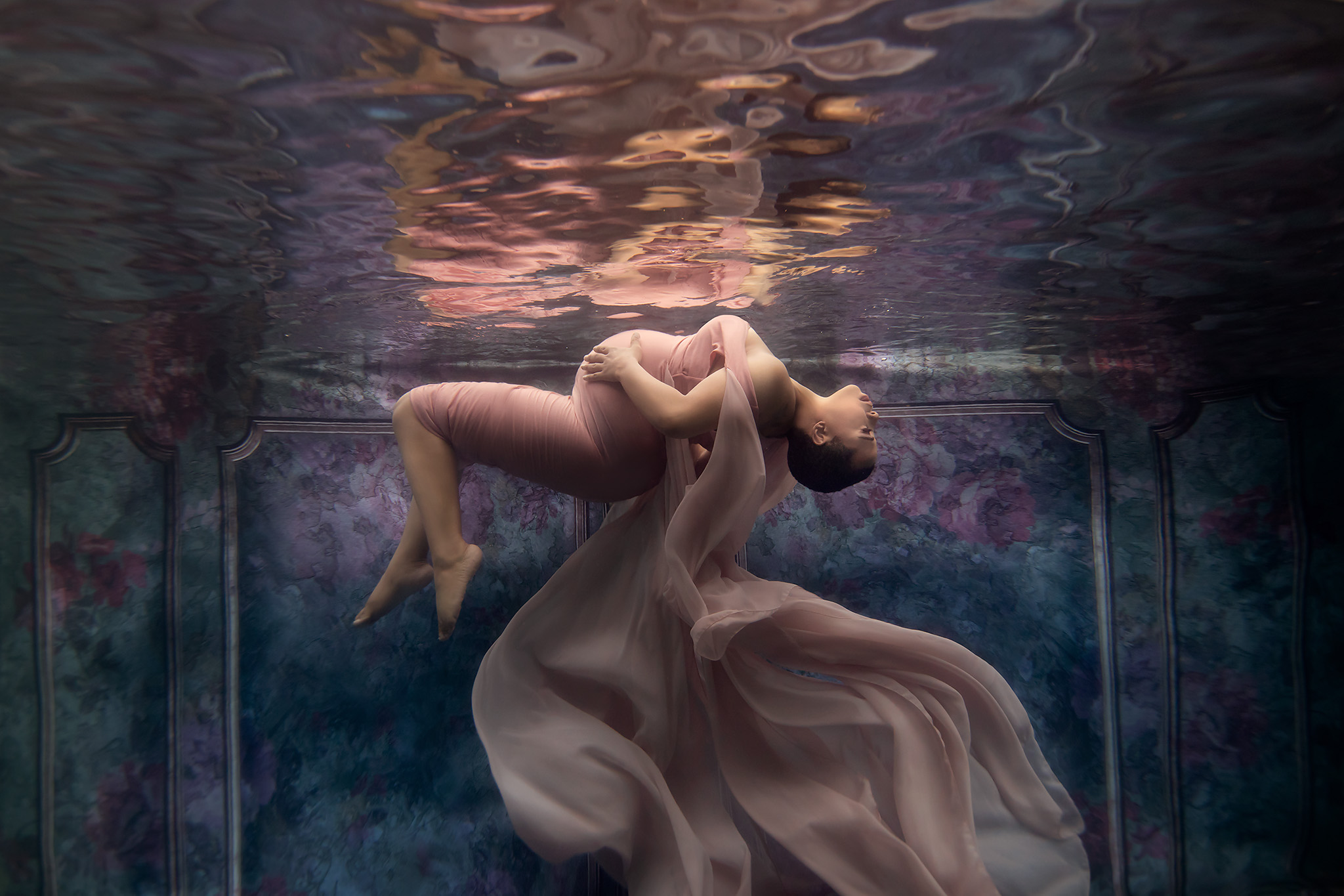 An incredible underwater maternity session with the client in a pink flowing dress appearing to float in a room