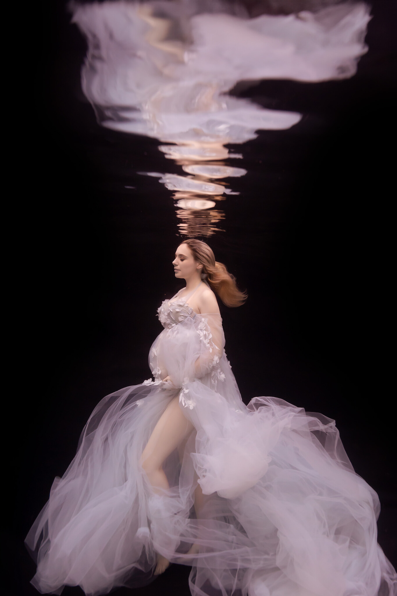Gorgeous underwater maternity session with pregnant woman in light blue gown in front of a black backdrop and her reflection above
