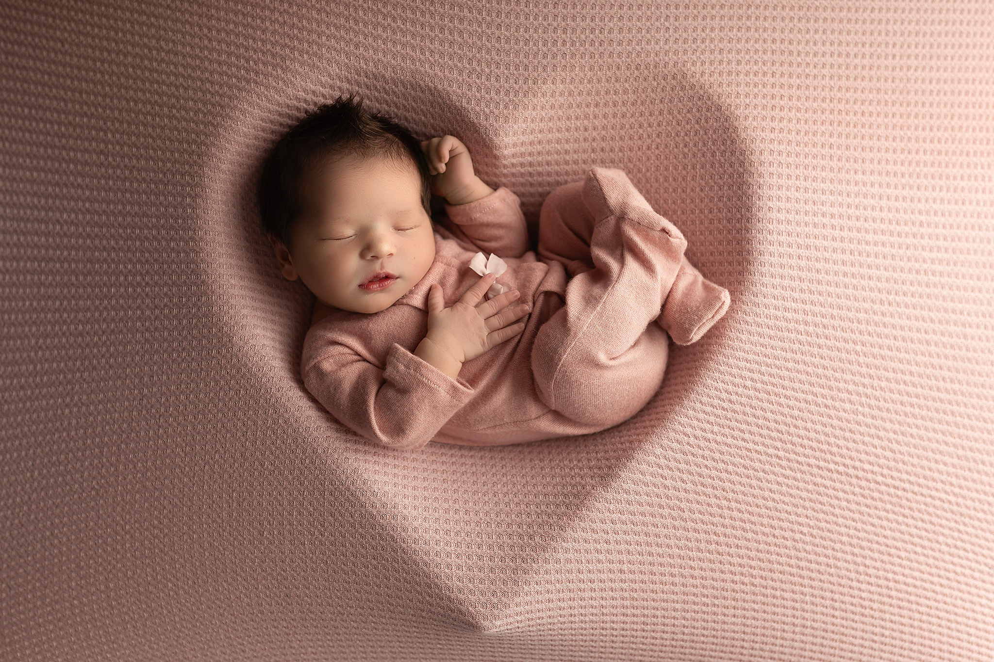 Baby girl in pink pjs laying in the shape of a heart on pink fabric the perfect example of a luxury newborn photoshoot in Dallas