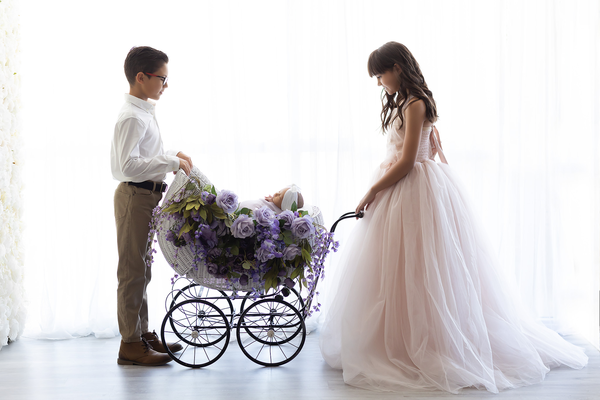 Preparing Older Siblings for Photos with a New Baby shows a boy and a girl standing on opposite sides of a vintage pram with a baby in it