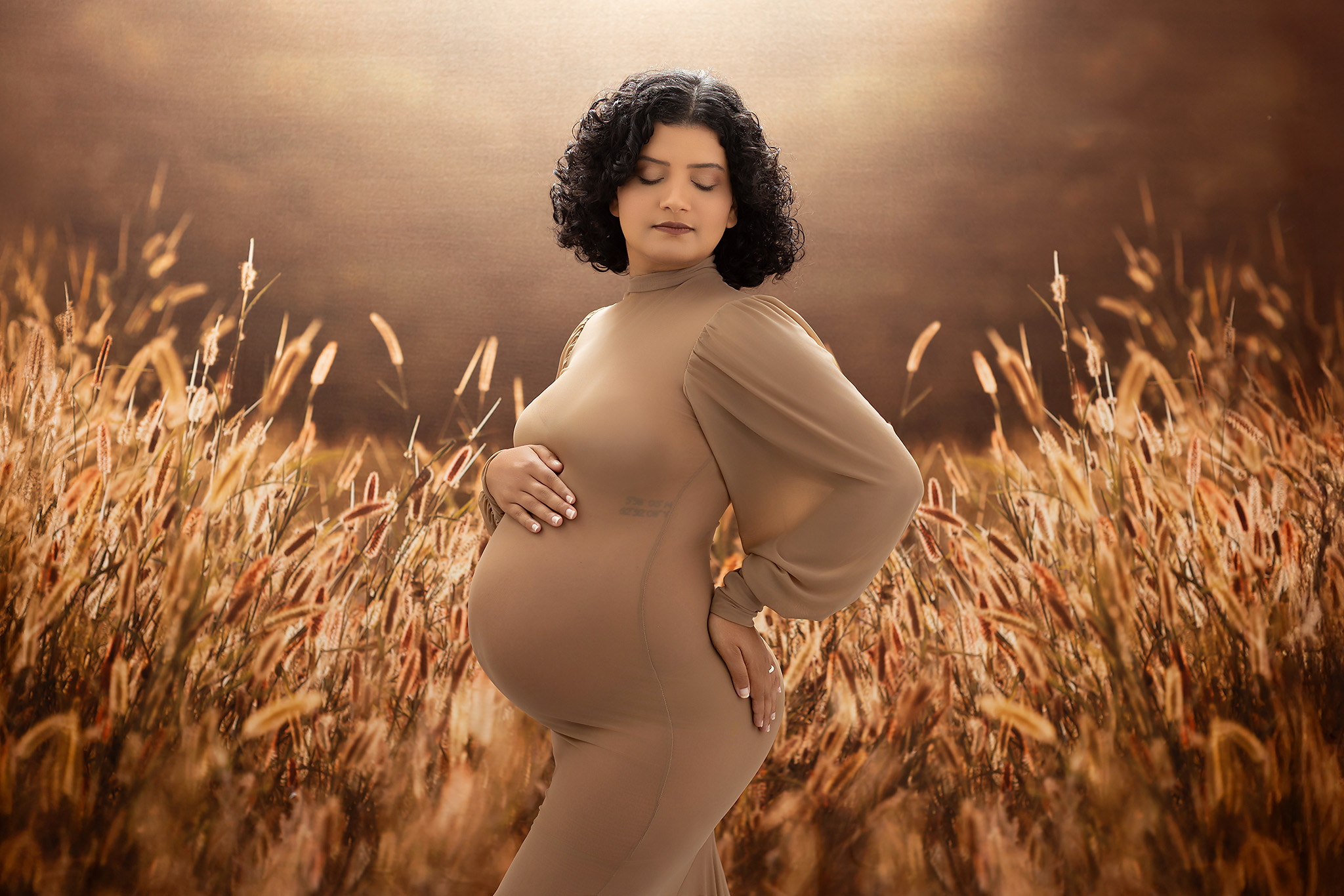Gorgeous pregnant woman standing in front of a wheat field with light coming from behind