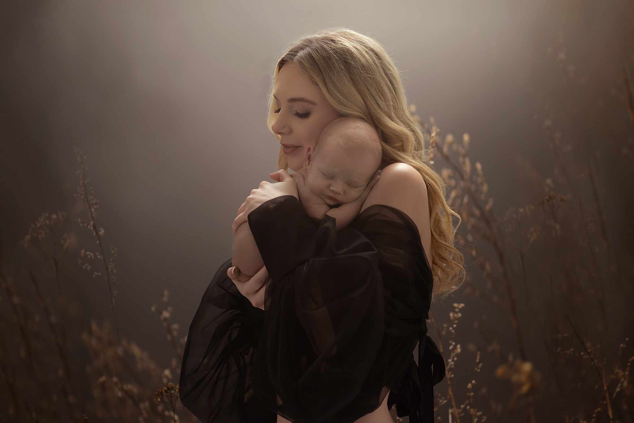 Mother holding her newborn baby in front of scattered flowers. The purposed of the image is to express why moms should be in photos.