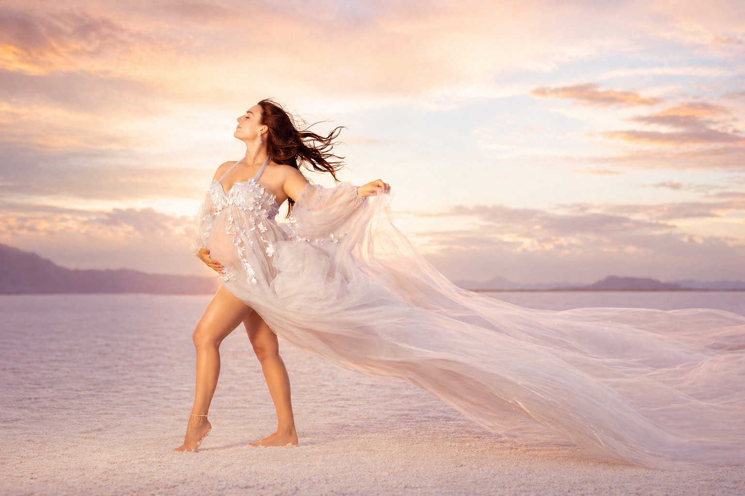 An expecting mom looking radiant in a blue tulle gown standing on salt flats with the sun setting behind and preparing for a luxury baby shower in Dallas
