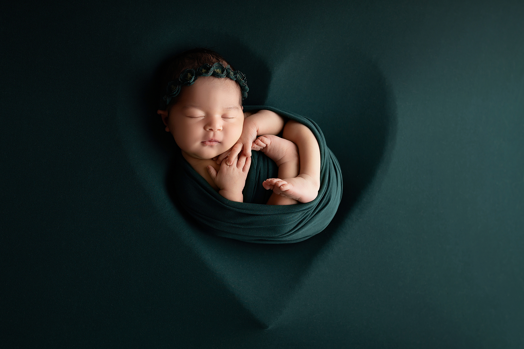 Newborn girl swaddled in green fabric in a heart shape. A cute idea for Baby registry guide for Dallas parents