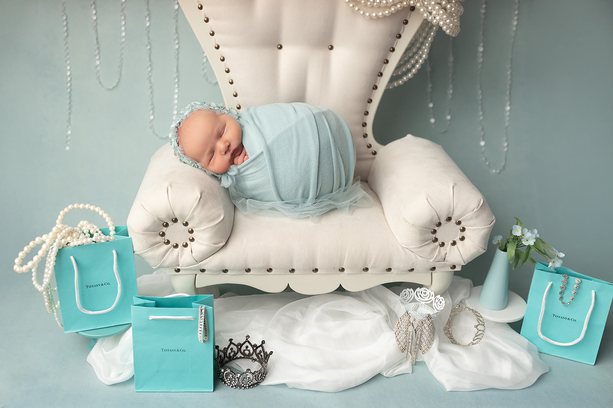 Newborn laid on white throne surrounded by jewelry and boxes. Find your luxury experience at baby boutiques Fort Worth.