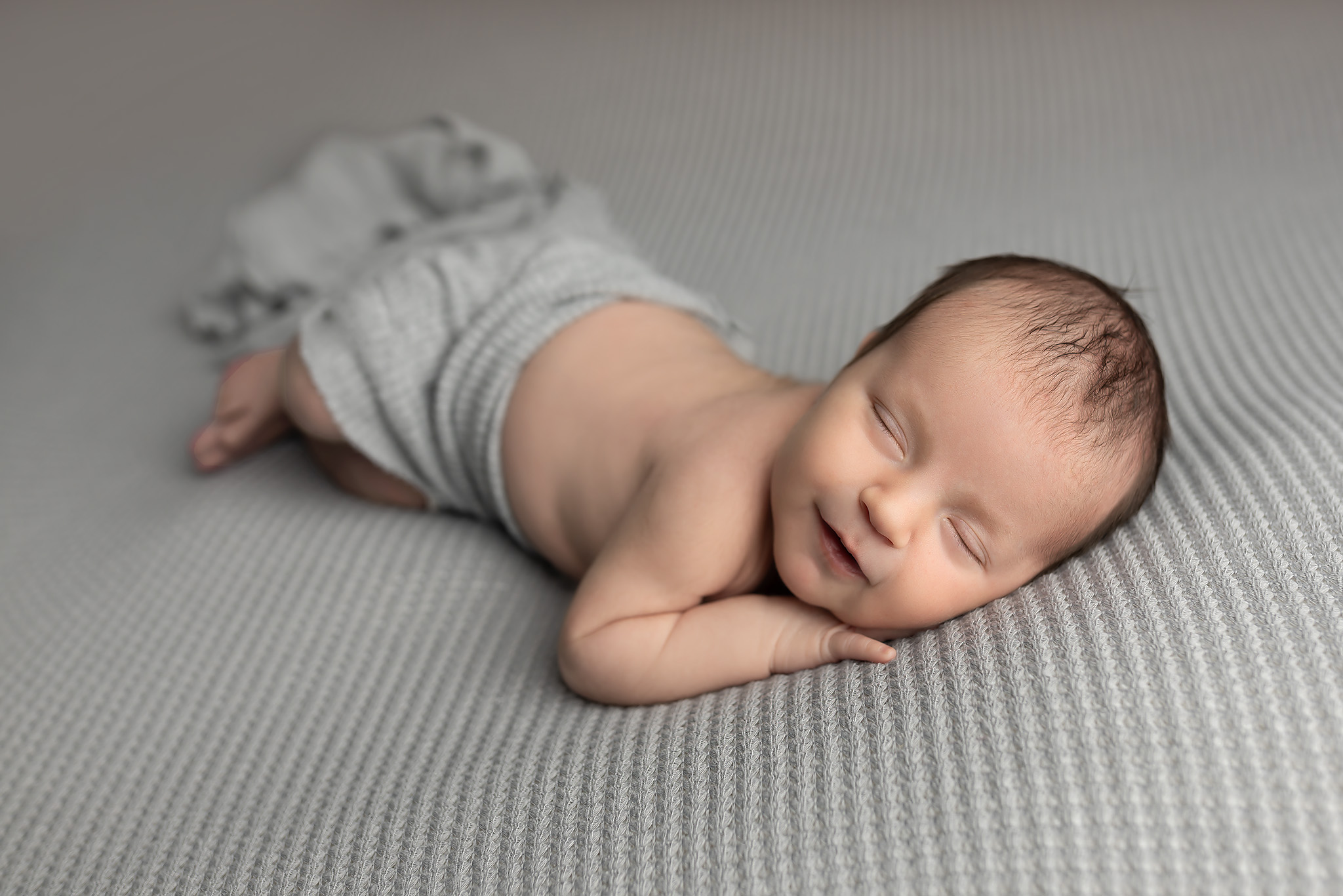 Baby smiling while laying on a cushy gray fabric.