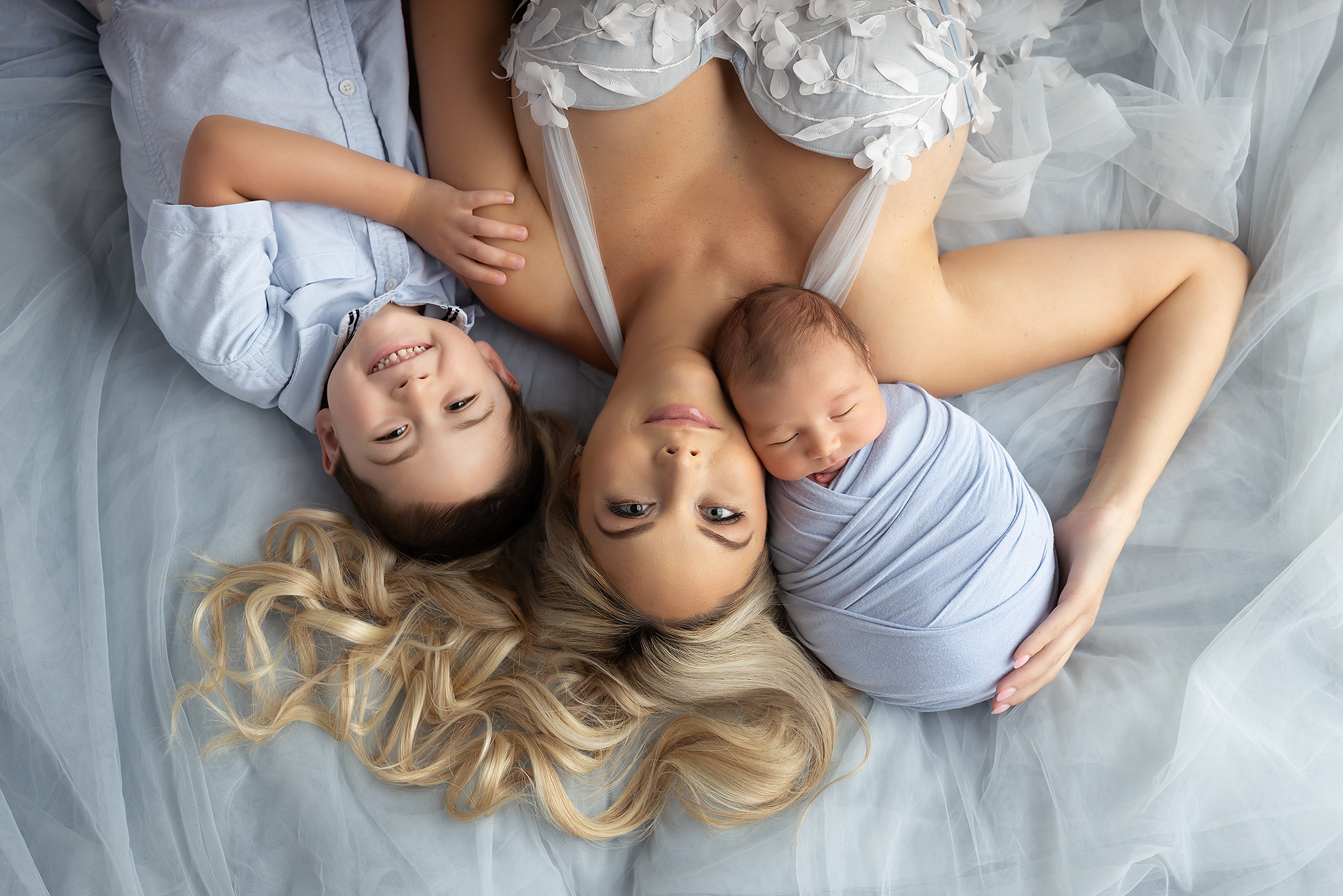 Mother and older son laying with baby on a light blue background.