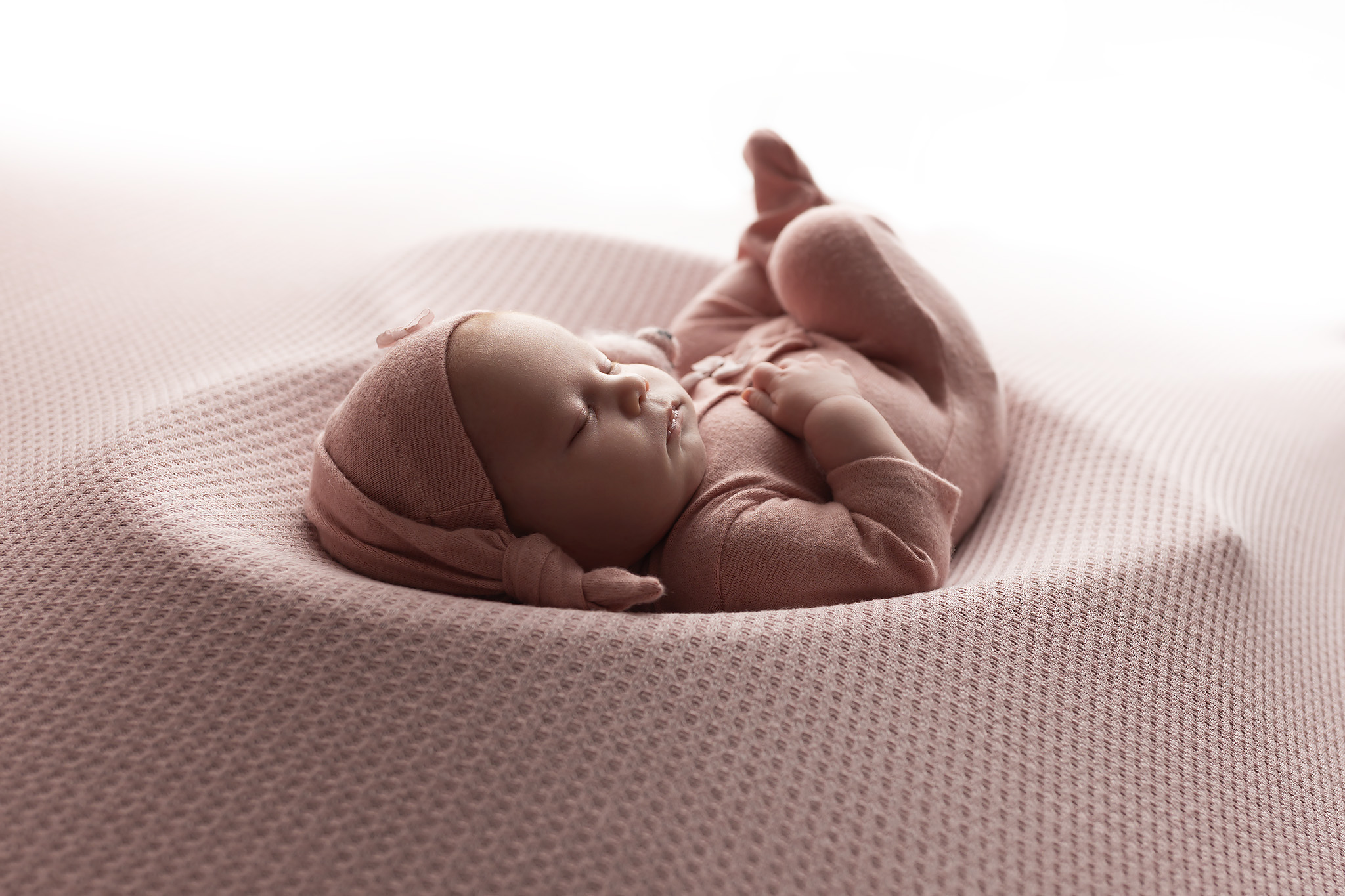 Baby sleeping in a pink heart bowl.