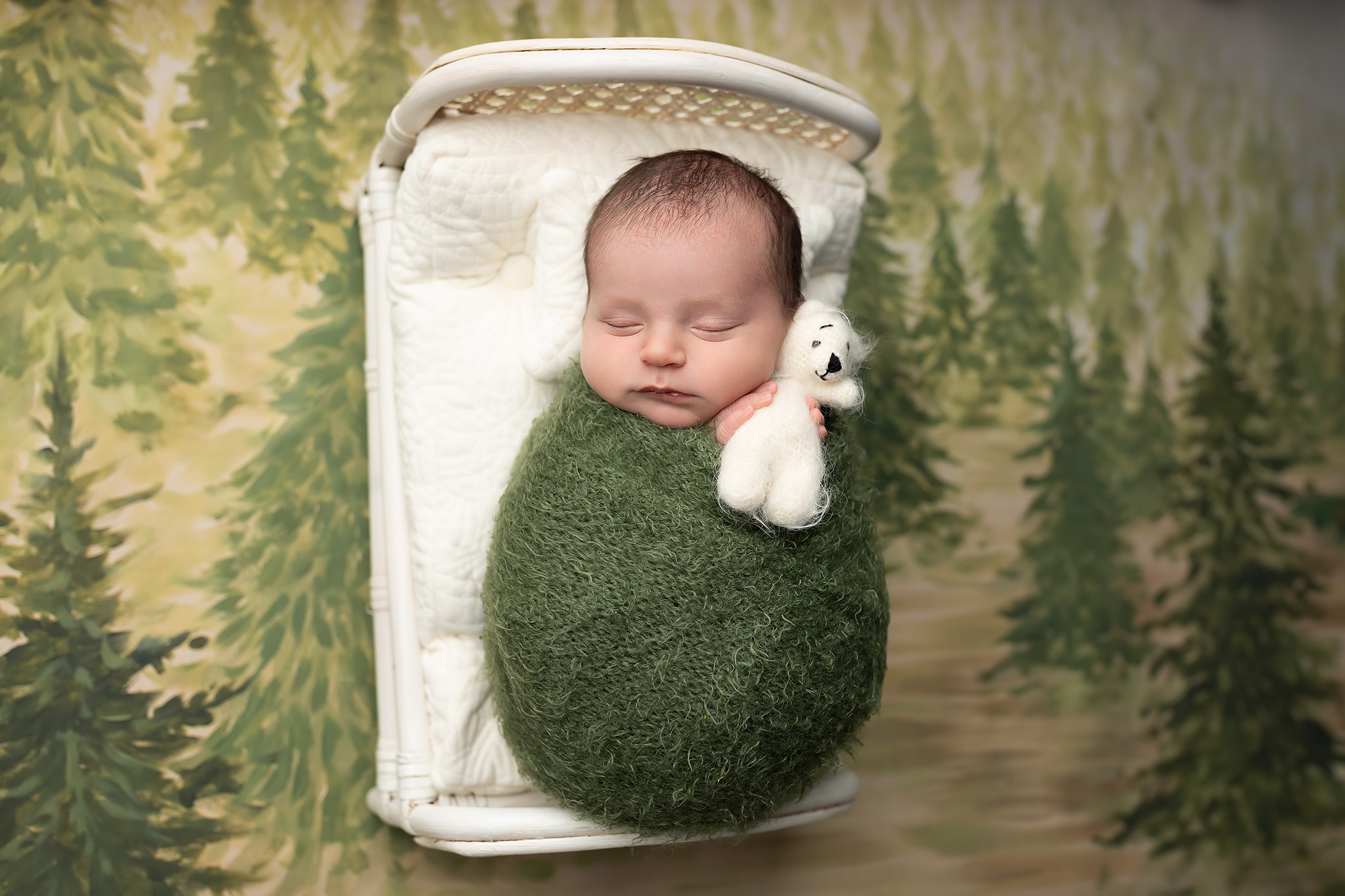 Baby wrapped in green holding a white teddy bear. Babyproofing services in Dallas